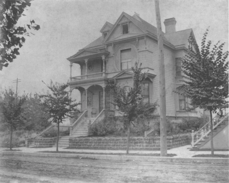 1895 B&W image of a grand Queen Anne Home road out front is dirt.