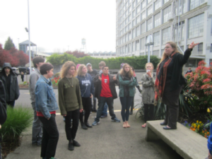 Group of high school age students on Slabtown walking tour. Tanya is standing on a bench ponying at Montgomery Park (once a Montgomery Ward regional center and department store currently the second largest office building in Portland). 