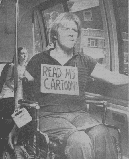 Callahan on a bus in 1984, he is in his wheel chair has a card board sign on his chest that says Read My Cartoon low quality newsprint