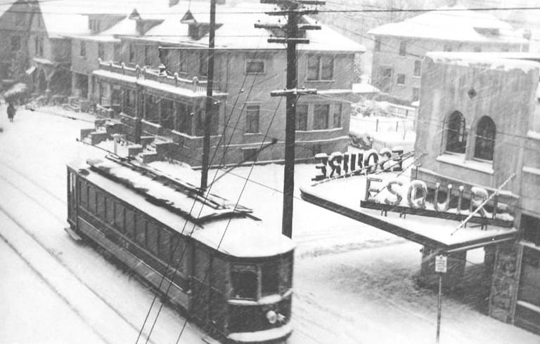 Snow story street screen taken from a second story apartment. Theater marque -Esquire- and a streetacr-trolly car.