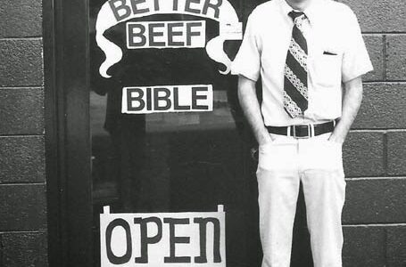 Image og Man in tie in front of his shop on 23rd, open sign is on door