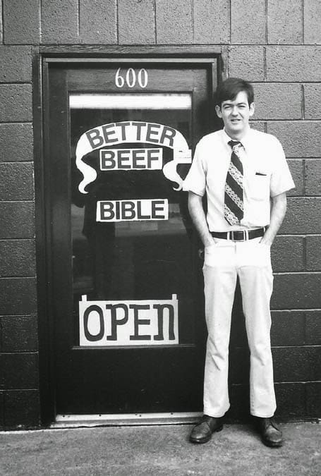 Image og Man in tie in front of his shop on 23rd, open sign is on door