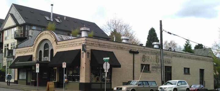 Image of theater. The building is a one-story brick structure. The front facade has an attractive set of three rounded windows framed by a rounded roof line. The side facade had a few windows and a fading ghost sign text "Ideal Theater"