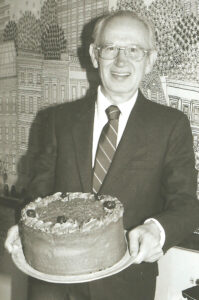 Max is wearing a suit the cake is an 8" round chocolate frosting no rises just four cherries on top.