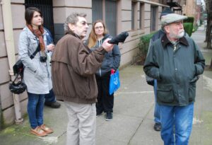 Mike Ryerson using his umbrella as a pointer,  Tanya and three tour guests are also pictured mid-walking tour