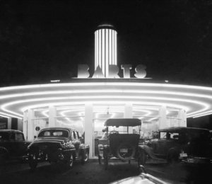 Image of 1940s Barts Drive-in. Black and white image with cars parked (waiting for car hops with food) there are about 70 plus feet of neon lights on the building looks like a space craft fressbee with an illuminated coit tower popped on top.