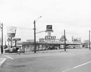 Old fast food drive in looks like a gas station on a wide street has a sign that is a giant size bucket of KFC chicken I assume in spins 