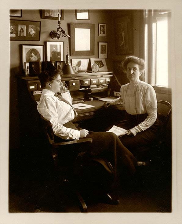 Two woman sepia tone with buns sitting at desks on the wall are sign pictures from the stars the company manages