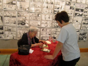 Ursula is signing a copy of Cat Wings for Brooklyn at Powells Books there are dozens of black and white pages pined to the wall behind them 