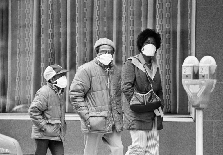 A Black child is walking down the street with what might be his parents they are all wearing masks the old style double headed parking meter ads a night balance to the image
