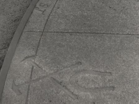 There is a metal band protecting a curved curb edge and when the cement was wet some une mad impressions of three items a horse shoe and two iron smith tools