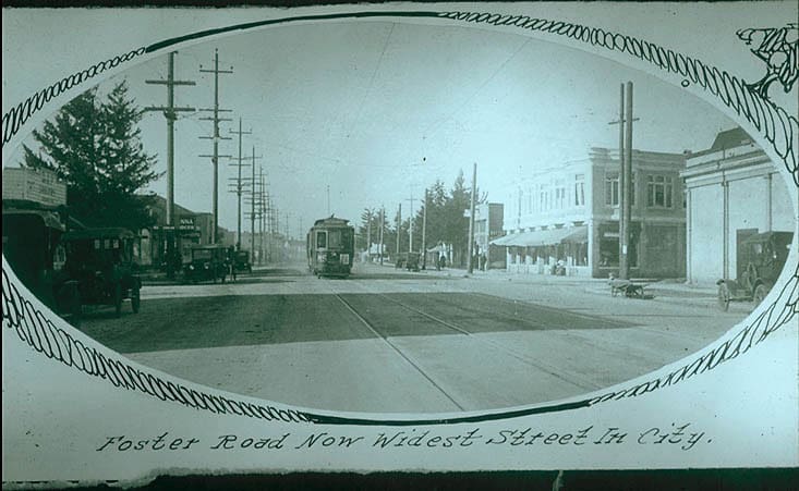 image has hand drand frame discolored shows stores on each side of foster can read signs fooster looks super wide maybe fish eye or as if and there is a street car heading towards camera man