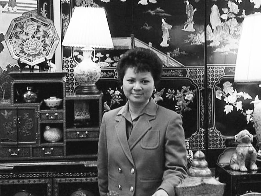 Image of a 40ish Chinese Woman within a shop full of Chines antiques of all kinds you notice the lamps because the bulbs are casting bright light.