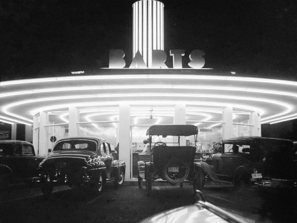 A circular drive in with rings of neon like Saturn's rings and a word BARTS in Block letters neon as well and a round tower with lines of neon. Te cars look antique picture is Black and white