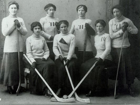 Seven woman in long wool shirts all have hockey sticks