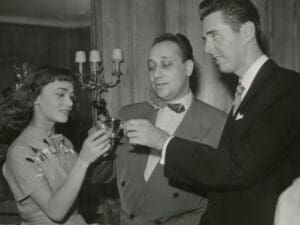 Movie star looking 19ish woman on the left with two gentle men that look more interested in undressing her than in the wine glasses they are holding