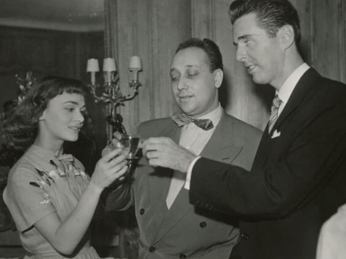 Movie star looking 19ish woman on the left with two gentle men that look more interested in undressing her than in the wine glasses they are holding